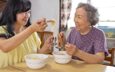 Happy elderly mother and daughter eating noodles at homeの写真素材