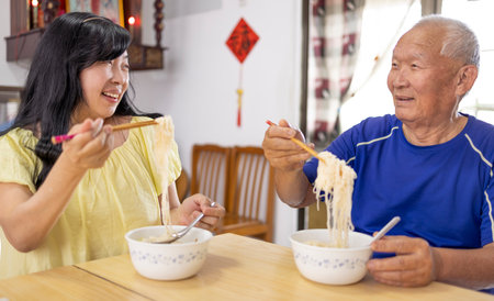 Happy elderly father and daughter eating noodles at homeの写真素材