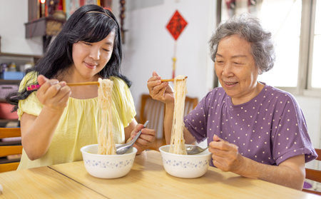 Happy senior mother and daughter eating noodles at homeの写真素材