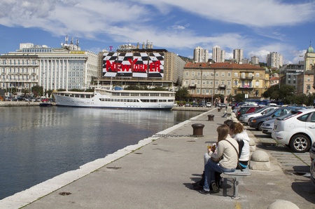 Rijeka, Croatia - April 5th 2011: View at the bussines buildings in Rijeka, Croatia from promenade in harbor. Girls sitting on the bench. visible big add for New Yorker.のeditorial素材