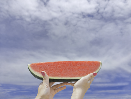 Women hands holding slice of watermelons on blue sky backgroundの写真素材