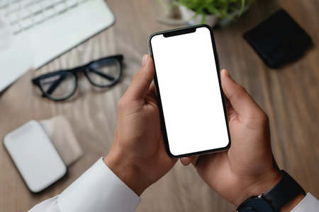 Cropped shot of businessman using smartphone with blank screen while sitting at modern office deskの素材