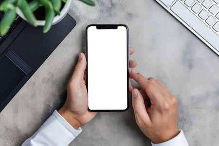 Cropped shot of businessman using smartphone with blank screen while sitting at modern office deskの素材