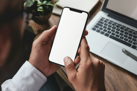 Cropped shot of businessman using smartphone with blank screen while sitting at modern office deskの素材