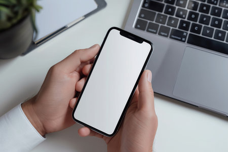 Cropped shot of businessman using smartphone with blank screen while sitting at modern office deskの素材