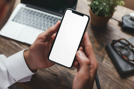 Cropped shot of businessman using smartphone with blank screen while sitting at modern office deskの素材