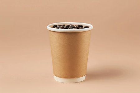 Takeaway paper coffee cup filled with black coffee, casting a soft shadow on a beige surface with natural lightの素材