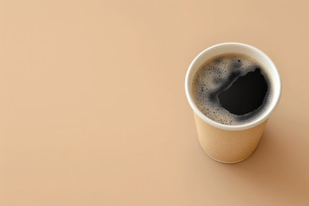 Takeaway paper coffee cup filled with black coffee, casting a soft shadow on a beige surface with natural lightの素材