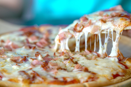 Close up af a hot pizza slice with dripping ham sausage and mozzarella cheese.の写真素材