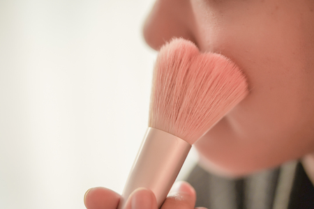 Pretty girl is applying blush on cheek by brush. Beauty Makeup.の写真素材