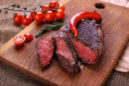 Well-done steak with chili pepper and cherry tomatoes on a wooden dish. Food photo for restaurant menuの写真素材