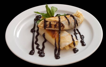 Plate of delicious crepes roll with fresh fruits and chocolate, isolated on black backgroundの写真素材