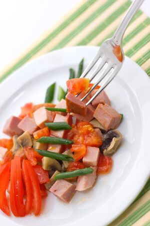 Delicious salad of ham, tomato, pepper and green onion on a white plate.の写真素材