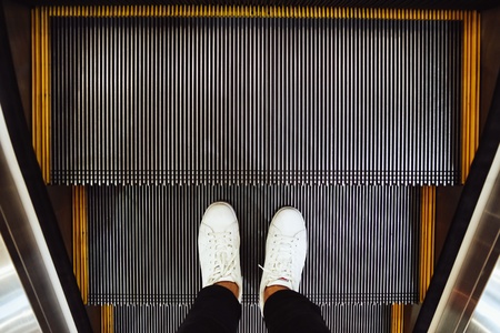 Selfie of  man feet in white sneaker shoes on escalator steps in the shopping mall, top view in vintage styleの写真素材
