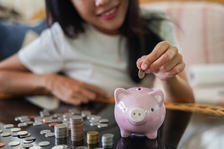 Happy young woman and hand putting coin into piggy bank, Finance or Savings concept.の写真素材