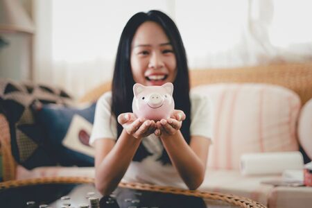 Young woman with pink piggy bank on hands and coins on table, Finance or Savings concept.の写真素材