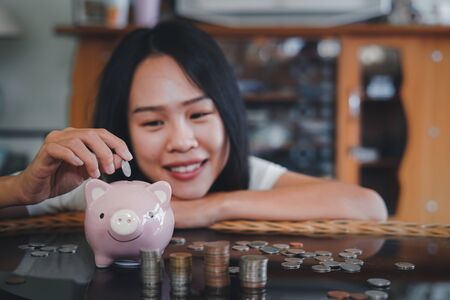 Happy young woman and hand putting coin into piggy bank, Finance or Savings concept.