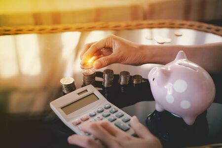 Hand putting coins in stack on a glass table with a piggy bank and counting on calculator, Finance or Savings concept.の写真素材