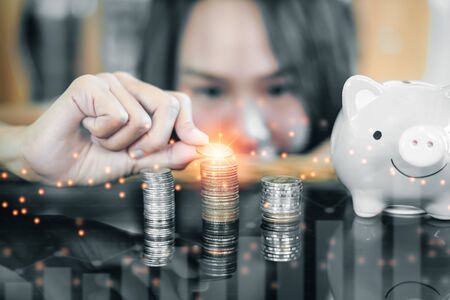 Woman hand putting coins in stack on a glass table with a piggy bank, Finance or Savings concept.の写真素材