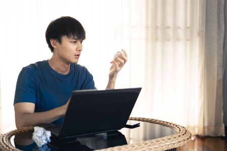 Man working on laptop computer in the room looking crumpled paper on hand, Concept of Work from home.の写真素材