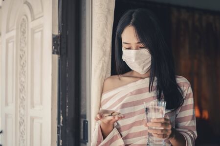 Young woman looking drug and wearing mask with medicine putting on hand and a glass of water, Pharmaceutical medicament, cure in container for health, Antibiotic, Medicine and health care concept.の写真素材