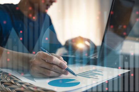 Double exposure of business man hands making notes with forex graph documents and looking stock in laptop computer on office table.の写真素材