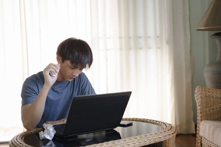 Handsome man looking computer screen and hand holding crumpling paper with work on laptop computer in the room, Work from home concept.の写真素材