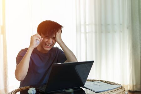 Angry crazy man Left hand holding head and right hand holding crumpling pape and yelled madly with work on laptop computer in the room, Work from home concept.の写真素材