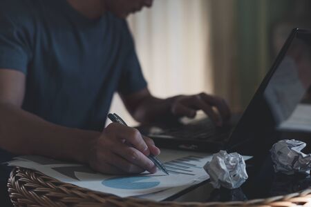 Man hand holding pen with graph and business documents on office table and working on laptop...