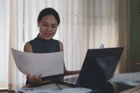 Happy woman smiling and hand holding paper documents and laptop computer in the office, Work at Home.の写真素材