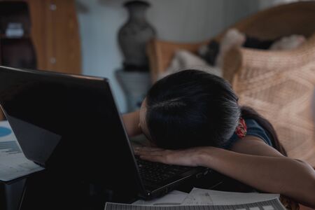 Asian business woman stressed and sleeping on laptop computer with graph documents on table, Work at Home.の写真素材