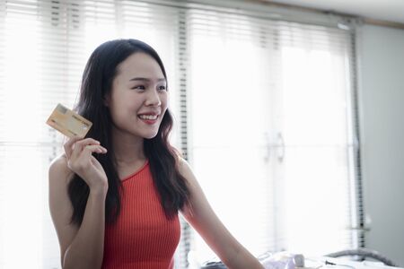 Asian beautiful young woman portrait in an orange vest with copy space she is smiling cheerfully and hand holding a credit card design for shopping online.の写真素材