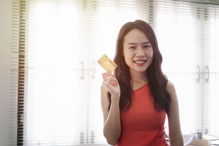 Asian beautiful young woman portrait in an orange vest with copy space she is smiling cheerfully and hand holding a credit card design for shopping online.の写真素材
