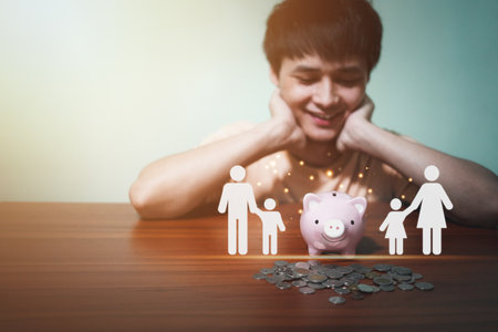 Handsome man is happy smiling and looking at icon family, piggy bank on table, donation, saving, charity, family finance plan concept, fundraising, superannuation, investment, finaの写真素材