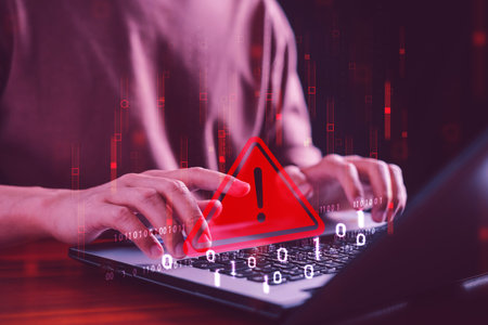 Hack system alert: A warning on the computer system indicates a cybersecurity threat or breach. A developer uses a laptop with a caution triangle sign, signaling an error and maintenance notification.の写真素材