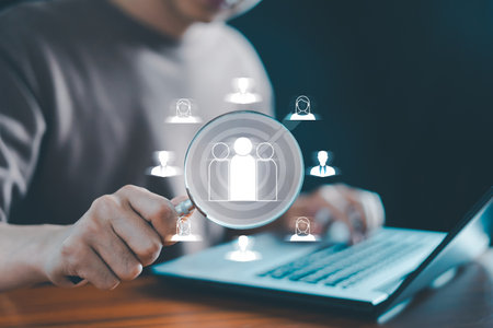 Business CRM (Customer Relationship Management) concept: A businessman uses a magnifying glass to search for a human icon, representing the focus on customer target groups, client management, and human resource management (HRM) within a business network.の写真素材