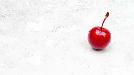 A vibrant red cherry sits alone on a textured white surface, showcasing its glossy skin and delicate stem. Perfect for illustrating freshness, health, and simplicity in food imagery.の素材