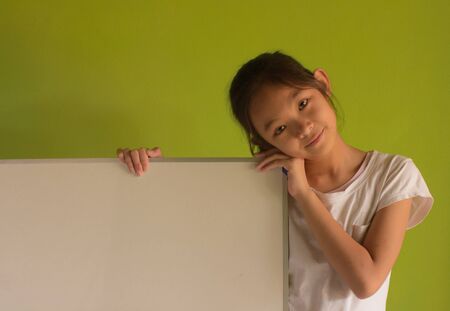 portrait girl wear white t-shirt holding a white board on green background.の写真素材