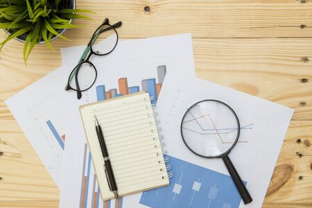 Office workplace with Magnifying glass on wood table,supplies and reports for analysis business planの写真素材