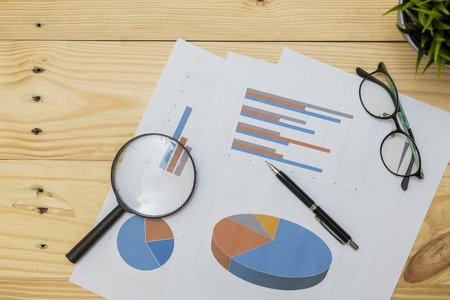 Office workplace with Magnifying glass on wood table,supplies and reports for analysis business plan