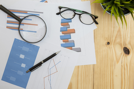 Office workplace with Magnifying glass on wood table,supplies and reports for analysis business planの写真素材