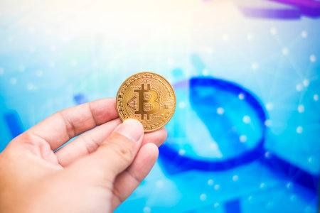 Close up man hand holding  bitcoin on a laptop with finance graphの写真素材