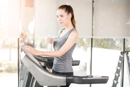 Pretty young sport woman is drinking water on treadmill in gym, Healthy lifestyle