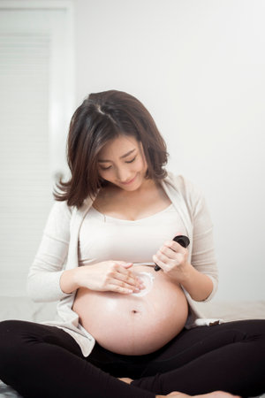 Close up of Pregnant woman applying cream at her belly