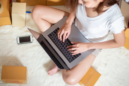 Woman entrepreneur owner SME business is checking order with smartphone, laptop and packaging box to...