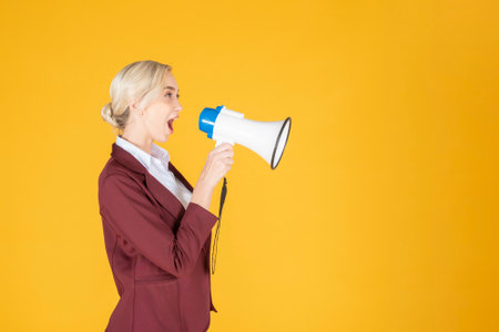 Business woman is announcing from megaphone on yellow backgroundの写真素材