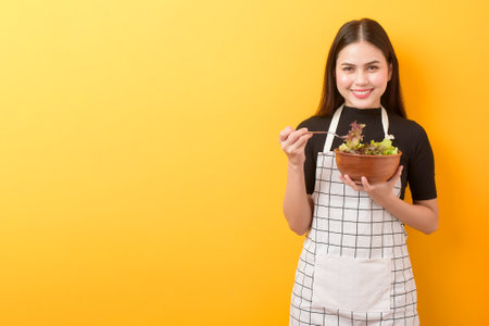 Beautiful healthy woman is eating vegetables on yellow backgroundの写真素材