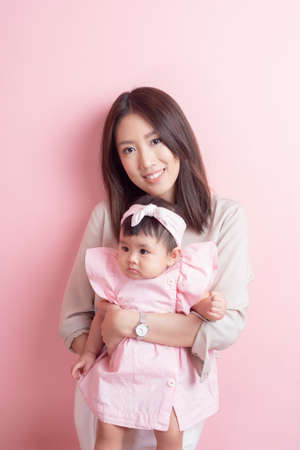 Asian mother and adorable baby girl are happy on pink backgroundの写真素材
