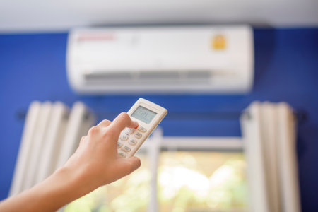 Woman is turning on air conditioner in homeの写真素材