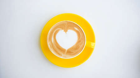 hot latte art in yellow cup on working deskの写真素材